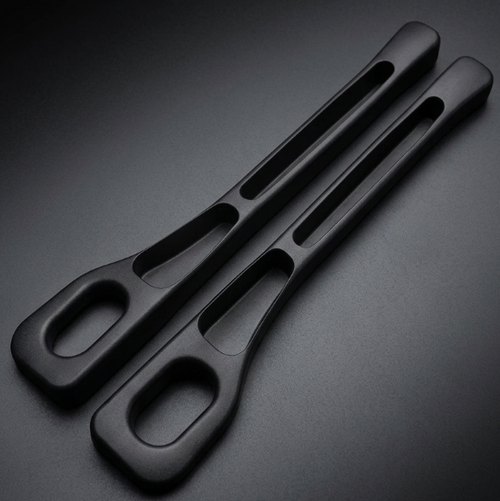 Two matte black ergonomic handles with integrated cutouts, photographed on a dark gradient studio background.